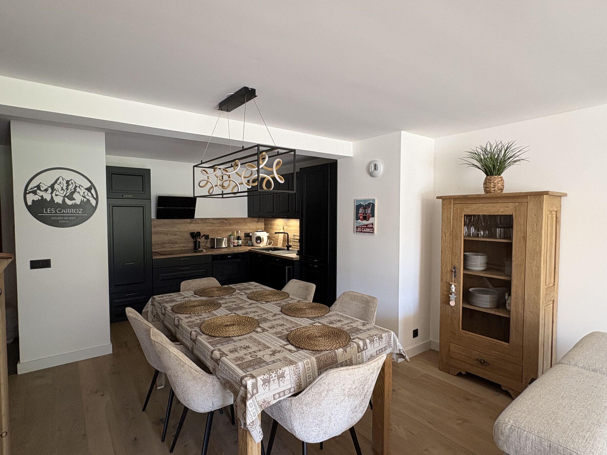 Un comedor con una mesa dispuesta para cuatro personas, una cocina al fondo y un armario con vajilla.