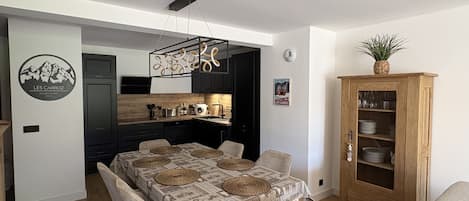 Un comedor con una mesa dispuesta para cuatro personas, una cocina al fondo y un armario con vajilla.