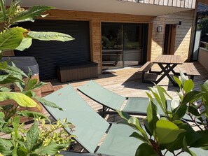 A wooden deck with outdoor furniture, including lounge chairs and a table, and a sliding glass door leading to an interior space. - Apartment with parking - 6 guests (Arâches-la-Frasse)
