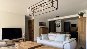 Ein Wohnzimmer mit Fernseher, Sofa, Couchtisch aus Holz und einer dekorativen Deckenleuchte.