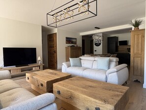 Ein Wohnzimmer mit Fernseher, Sofa, Couchtisch aus Holz und einer dekorativen Deckenleuchte.