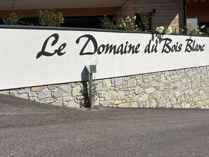 A sign for 'Le Domaine du Bois Blanc' with a stone wall and a metal pole. - Apartment with parking - 6 guests (Arâches-la-Frasse)