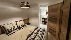 Ein Schlafzimmer mit einem Bett, einem Nachttisch, einem Holzschrank und einem durch eine offene Tür einsehbarer Badezimmer.