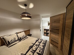 Ein Schlafzimmer mit einem Bett, einem Nachttisch, einem Holzschrank und einem durch eine offene Tür einsehbarer Badezimmer.