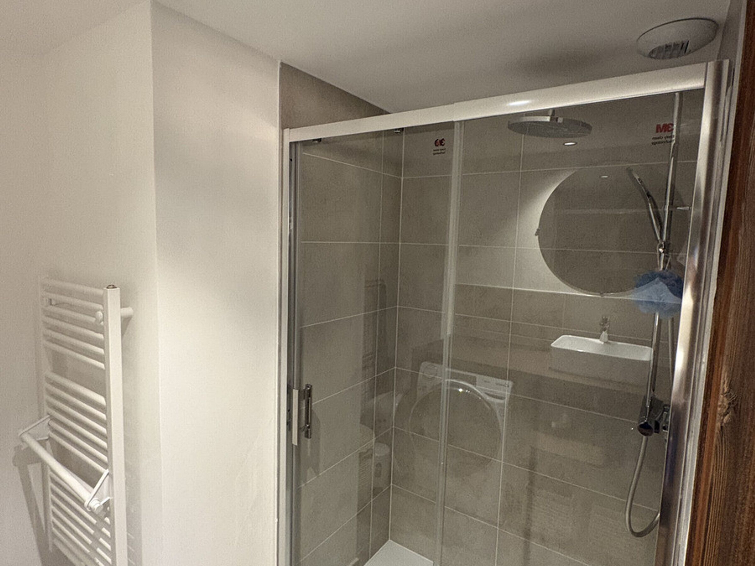 A glass-enclosed shower with a handheld showerhead, a glass door, and a white towel rack to the left.