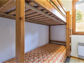 Uma cama beliche com colchão estampado, vigas de madeira e uma janela com vista para o verde.