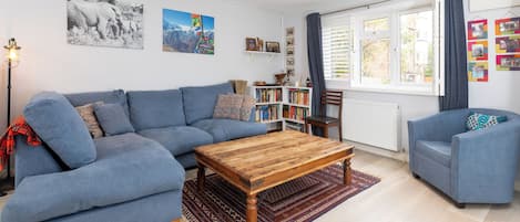 A living room with a blue sofa, a wooden coffee table, a bookshelf, and a window with curtains.