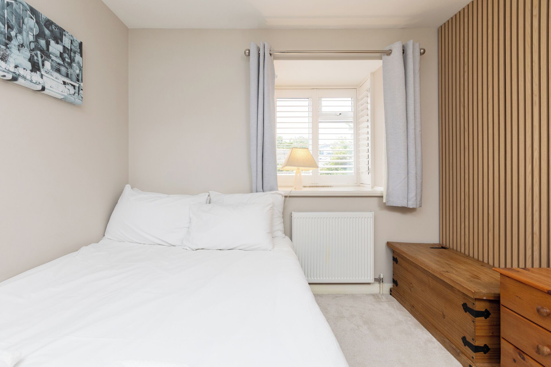 A bedroom with a bed, a radiator, a wooden dresser, and a window with curtains.