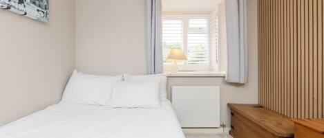 A bedroom with a bed, a radiator, a wooden dresser, and a window with curtains.
