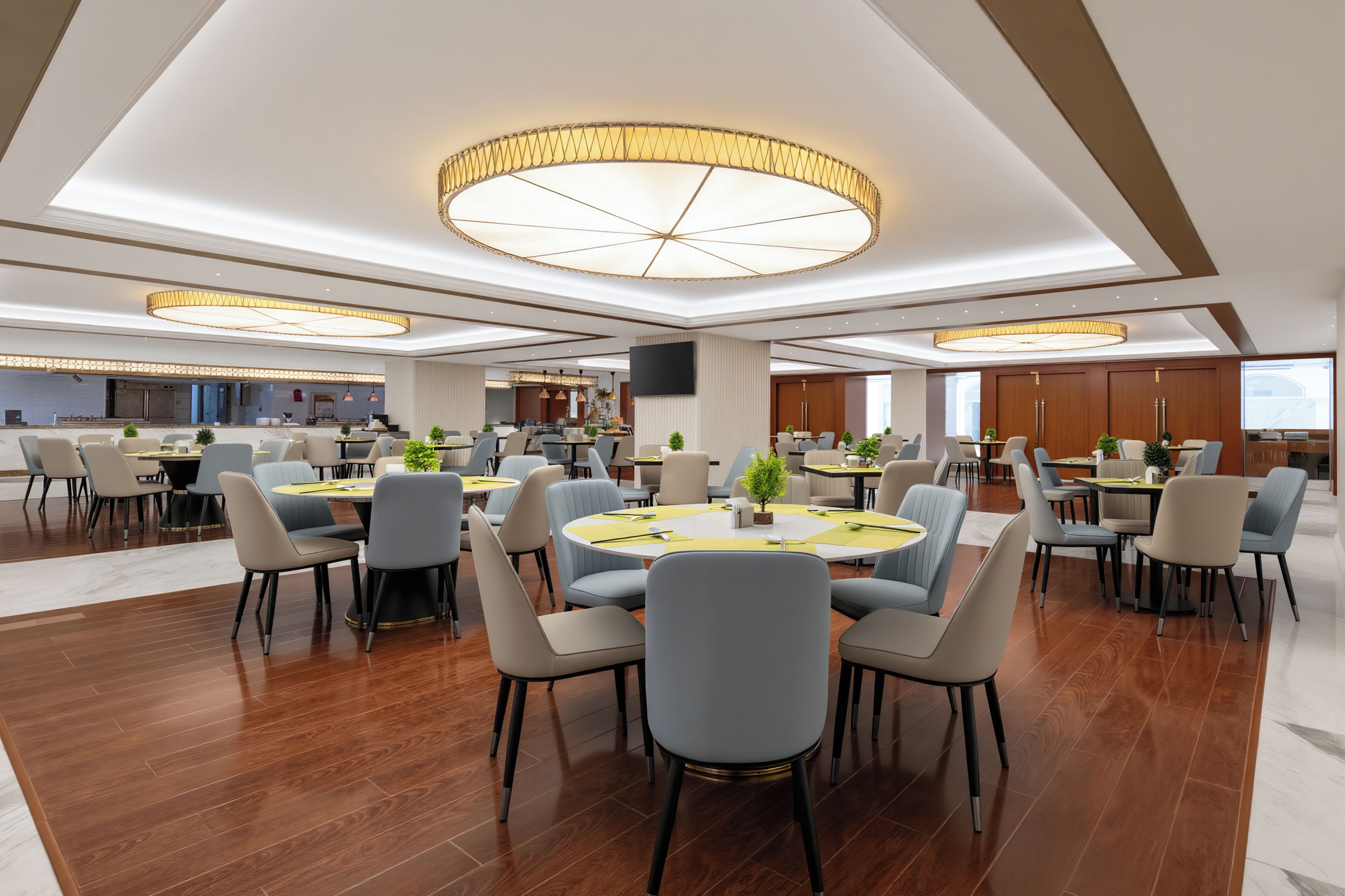 Un vaste espace dédié à la salle à manger, avec des tables rondes et des chaises modernes, agrémenté d’un lustre central et d’un grand téléviseur à écran plat fixé au mur.