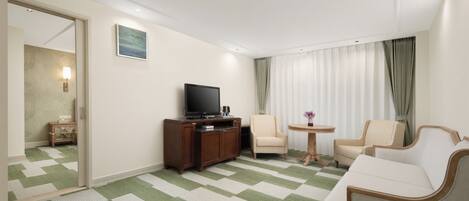 Une chambre d’hôtel équipée d’une télévision, de deux fauteuils, d’une petite table et d’un tapis à carreaux verts et blancs.