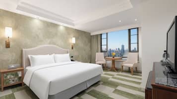 Habitación de hotel con una cama grande, dos mesitas de noche, un escritorio con una silla, un televisor y vistas a un horizonte urbano.