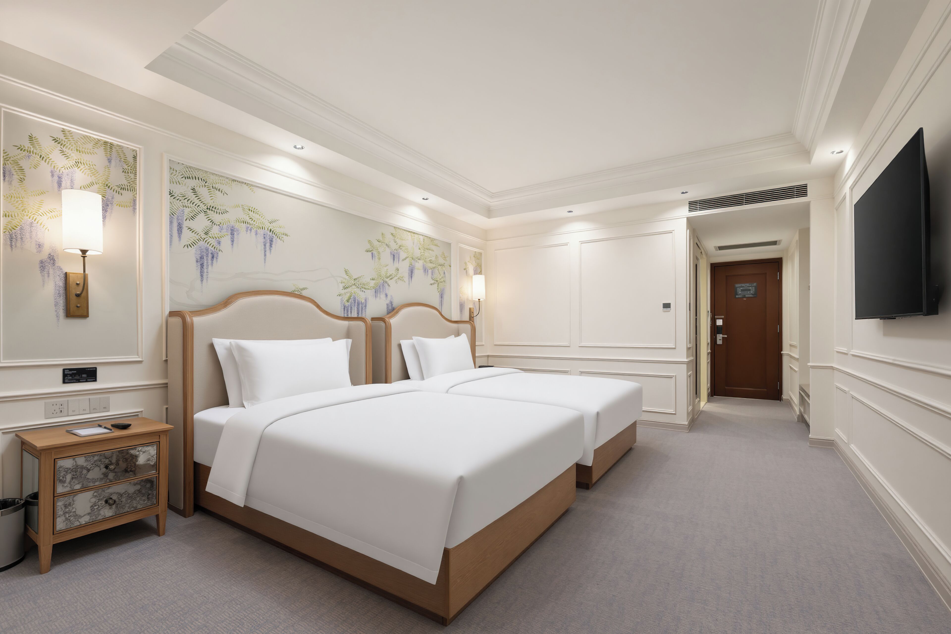 Une chambre d’hôtel avec deux lits, une table de chevet, un téléviseur et un mur orné d’une fresque florale.