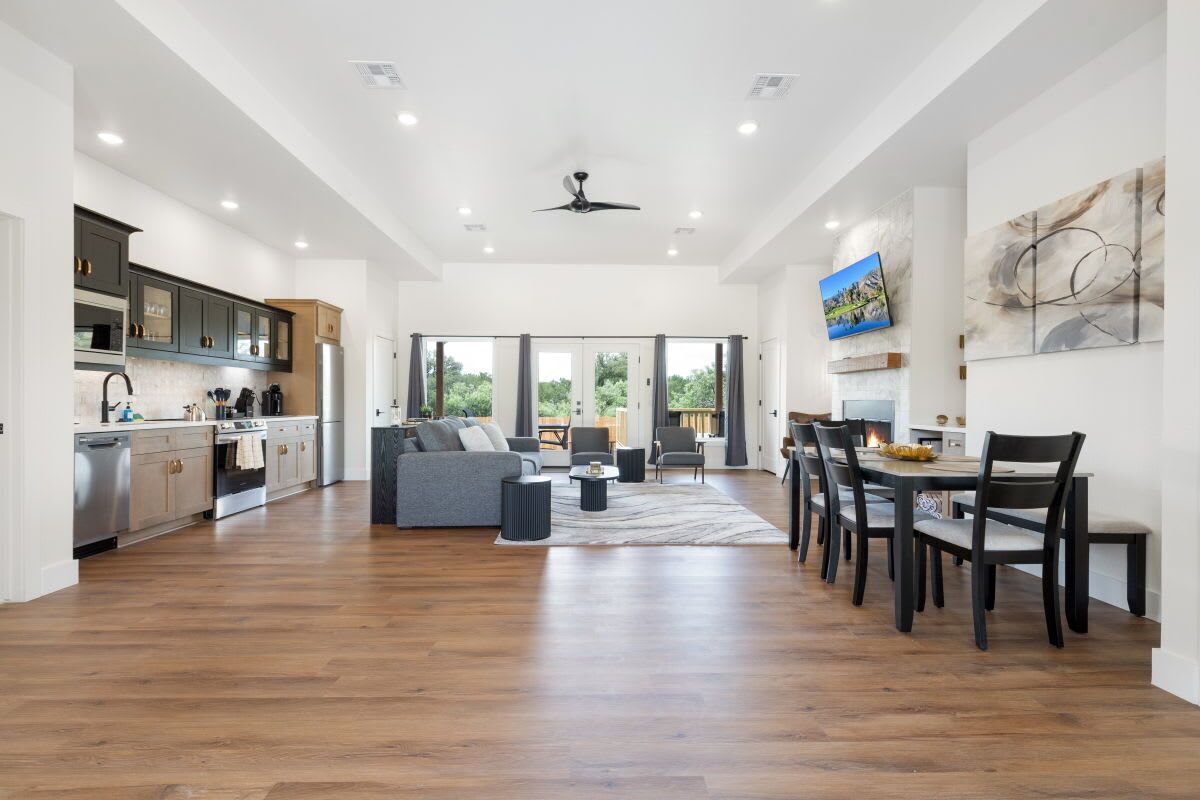 A spacious kitchen with modern appliances, a dining area with wooden chairs, and a large window offering a view of greenery.