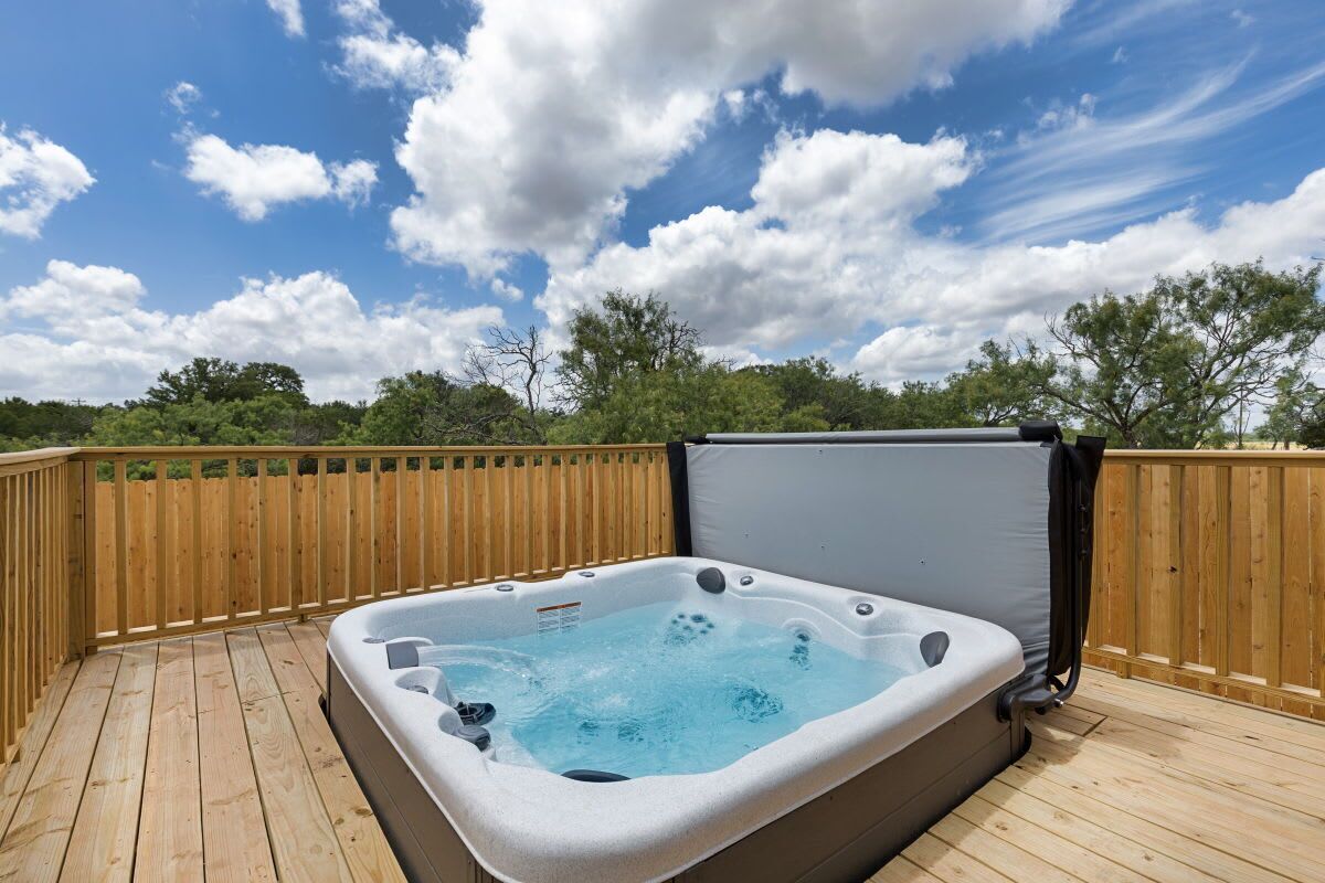 A hot tub on a wooden deck with a wooden fence and trees in the background.
