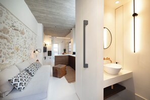 A modern interior with a stone wall, a white sofa with patterned cushions, a wooden coffee table, and a bathroom with a white sink and mirror. - Ligres DownTown (Rethymno)