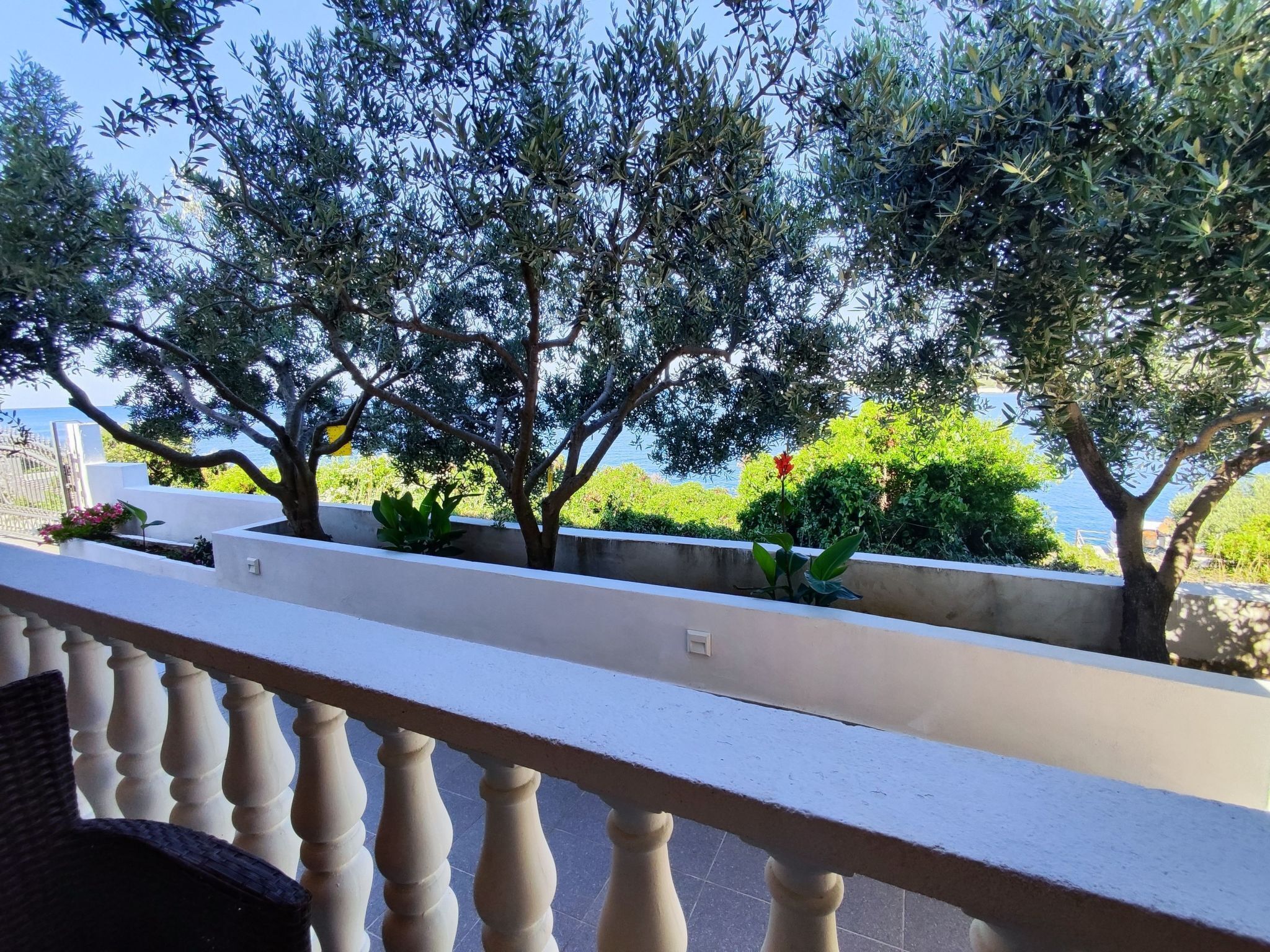 Un balcon doté d’une balustrade, donnant sur un jardin planté d’oliviers et offrant une vue sur la mer.