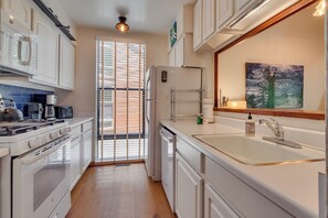 Una cocina moderna con muebles blancos, horno empotrado, lavamanos y ventana con persianas.