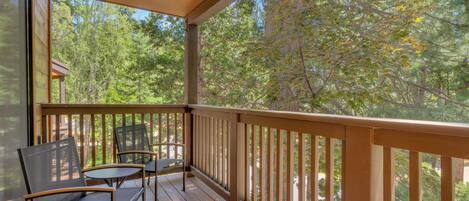 A wooden deck with a table and chairs, overlooking a forested area.