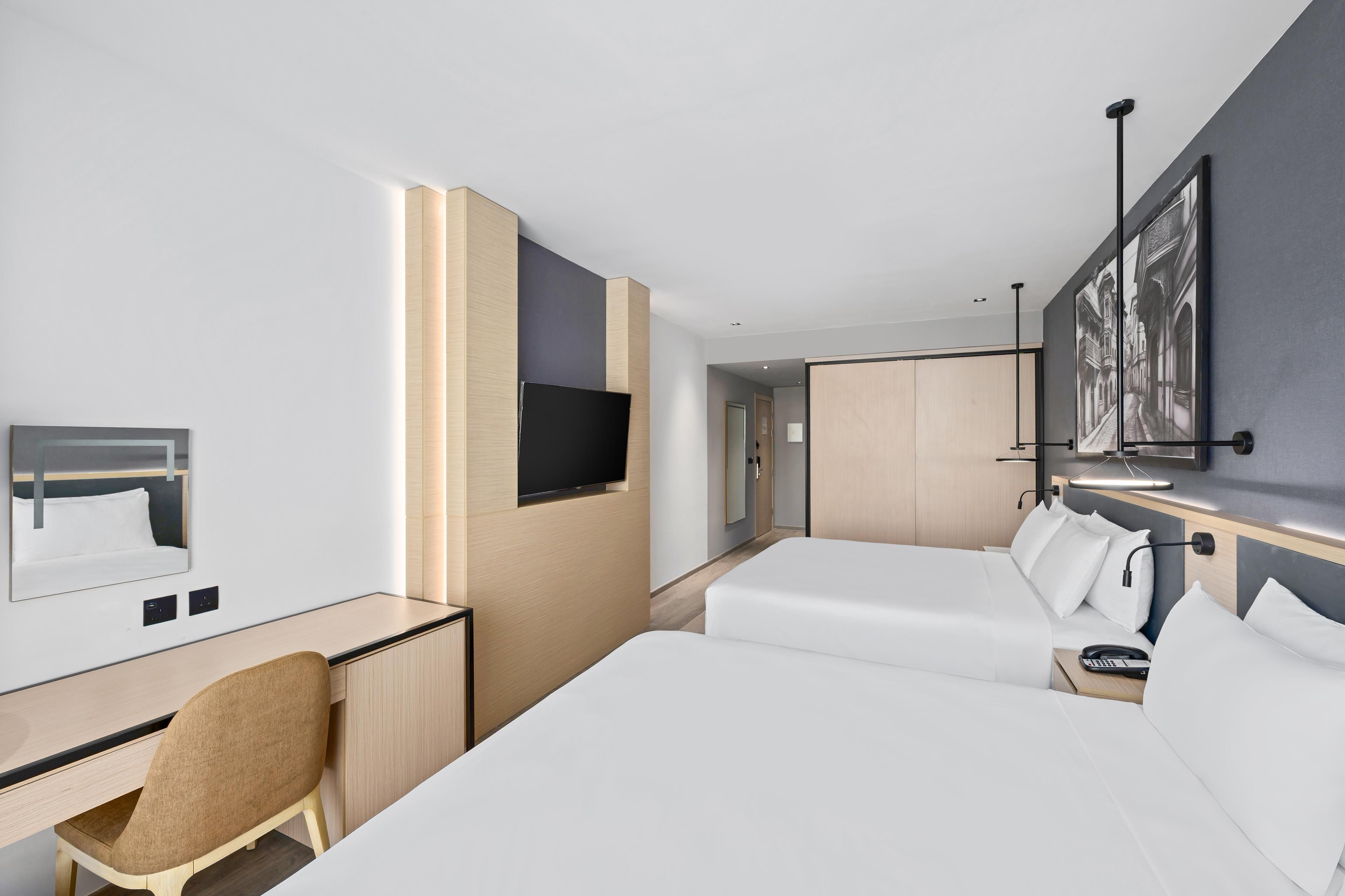 Een hotelkamer met een bureau, twee bedden, een televisie en een schilderij aan de muur.