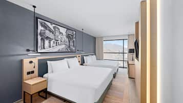 Habitación de hotel con una cama grande, mesitas de noche, un escritorio, un televisor y vistas a la ciudad.