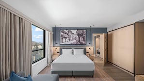 Una camera d'albergo moderna con un letto grande, vista sulla città e un quadro appeso al muro.