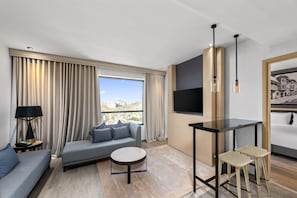 Quarto de hotel moderno com sofá, uma mesa redonda pequena, televisão e um quadro.
