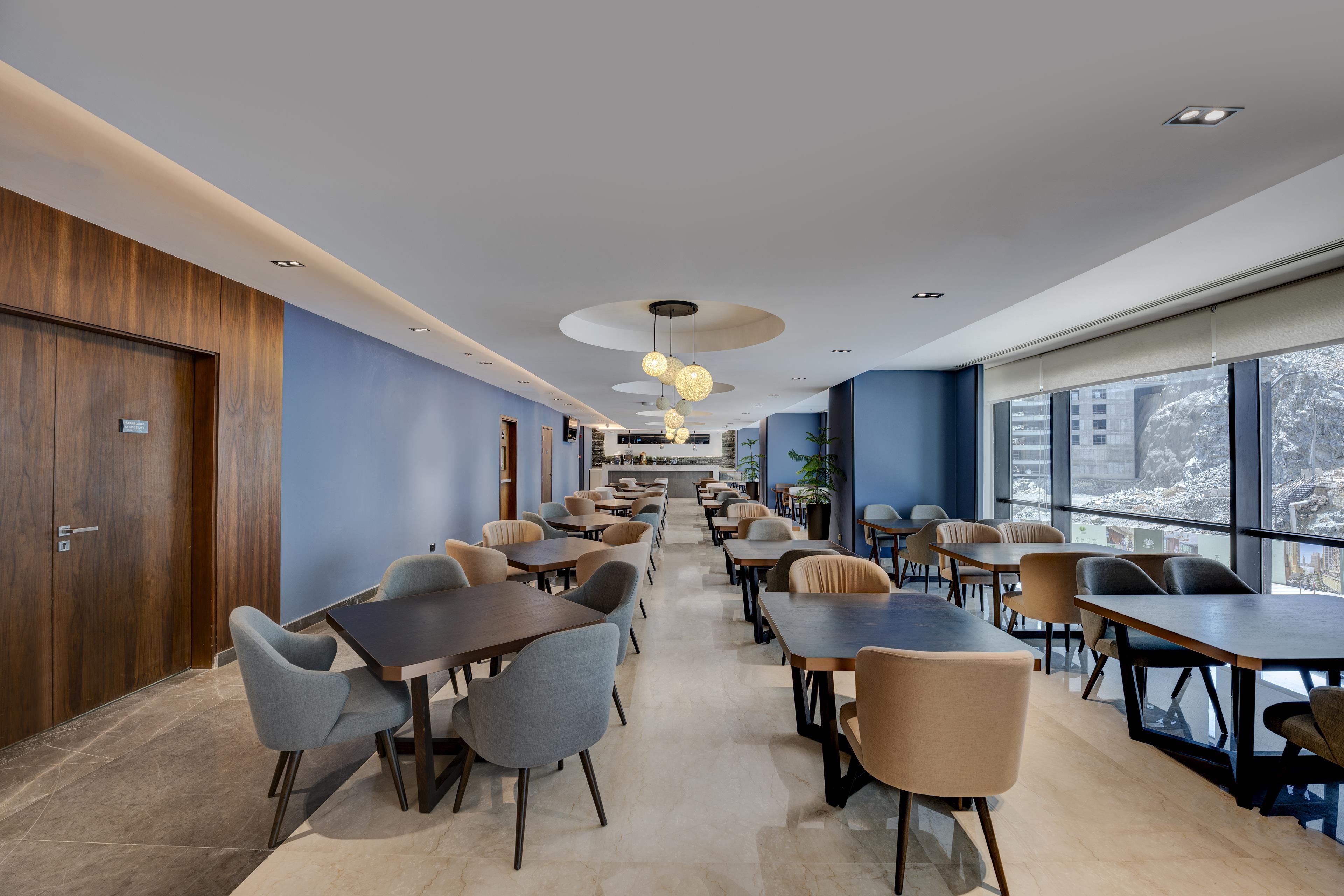 A modern dining area with multiple tables and chairs, a wooden wall on one side, and large windows on the other.
