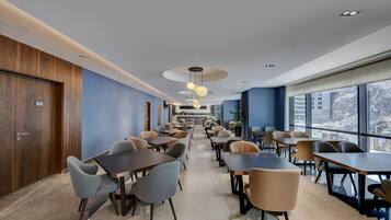 A modern dining area with multiple tables and chairs, a wooden wall on one side, and large windows on the other.