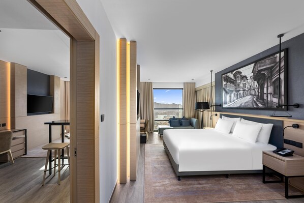 Una habitación de hotel moderna con una cama grande, un escritorio, una silla, un televisor y un cuadro en la pared.