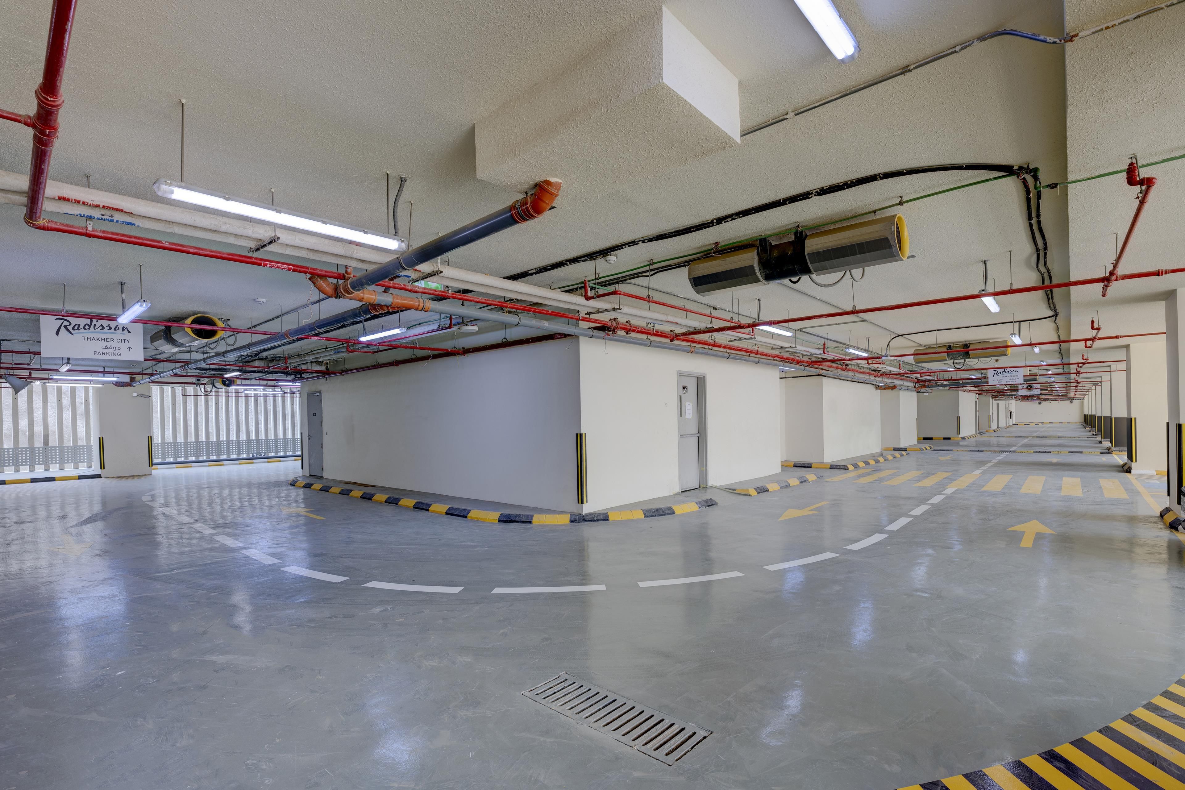 A parking garage with clear directional arrows on the floor, a sign indicating Radisson parking, and various pipes and ducts on the ceiling.