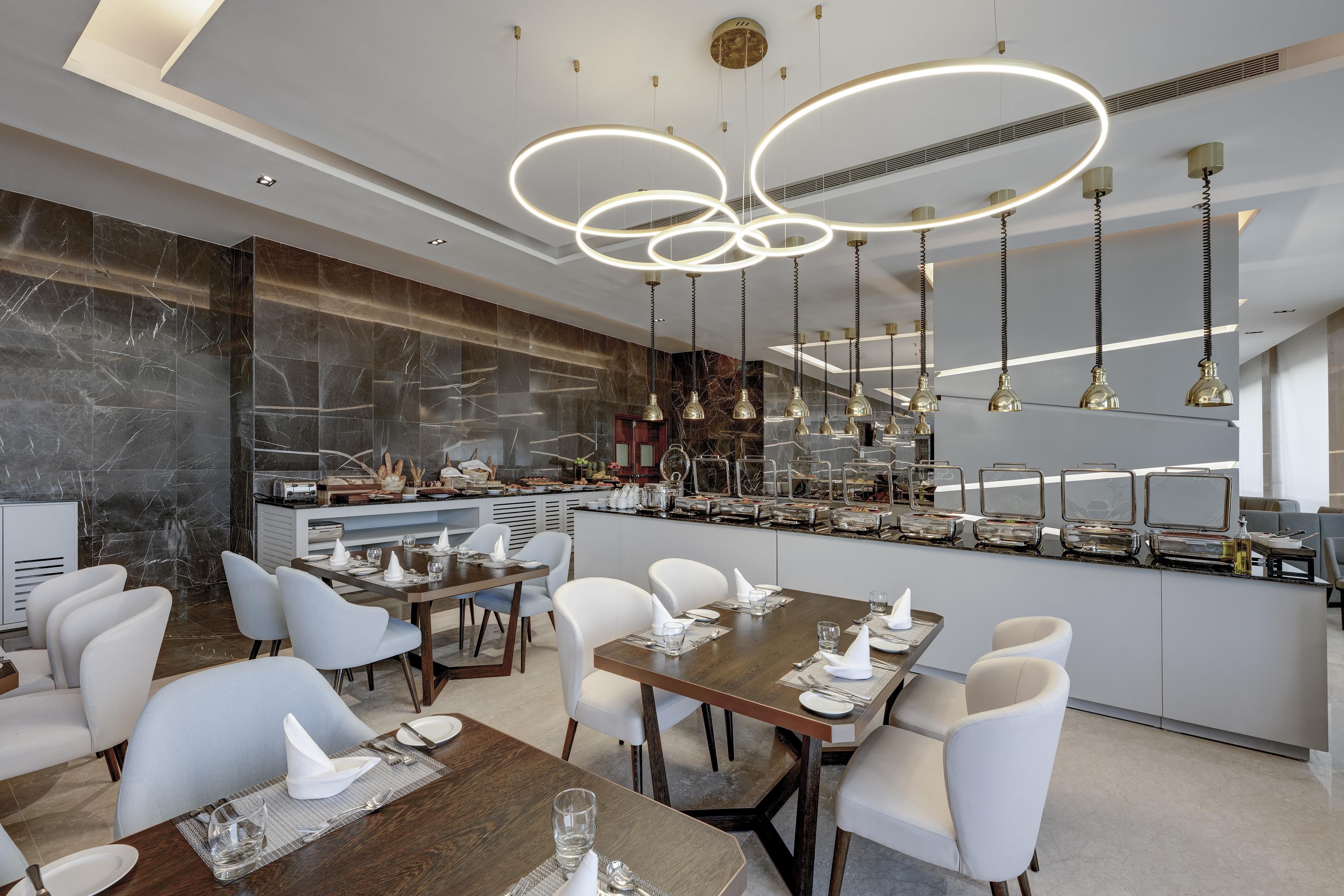 Uma sala de jantar moderna com painel de mármore, um buffet com diversos alimentos e um lustre contemporâneo.