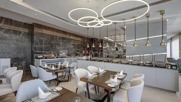 Uma sala de jantar moderna com painel de mármore, um buffet com diversos alimentos e um lustre contemporâneo.
