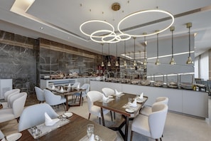 Uma sala de jantar moderna com painel de mármore, um buffet com diversos alimentos e um lustre contemporâneo.