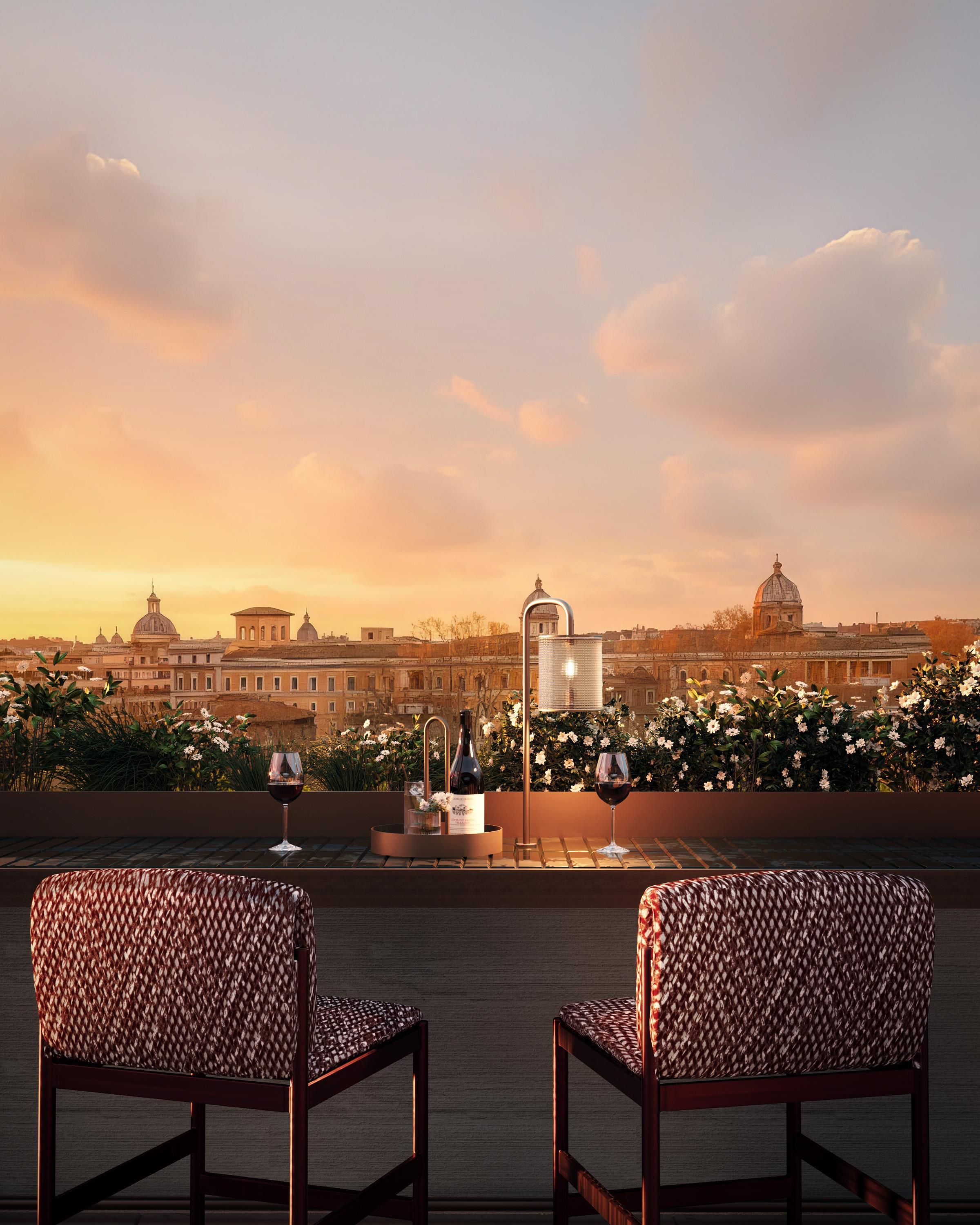 Una terraza con dos sillas estampadas, una mesa con una copa y una botella de vino, y vistas a edificios históricos.