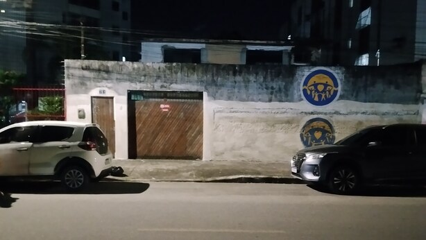Eine belebte Straße bei Nacht mit zwei parkenden Autos, einem Gebäude mit einer Tür und einer Wand mit einem kreisförmigen Emblem.