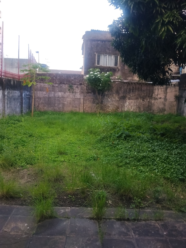 A grassy area with a concrete wall and a building in the background. - Hospedagem Simples Para Descanso  (Recife)