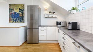 Eine moderne Küche mit einem Edelstahl-Kühlschrank, weißen Schränken, einer Mikrowelle und einer Kaffeemaschine auf der Arbeitsfläche.