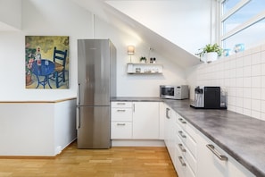 Eine moderne Küche mit einem Edelstahl-Kühlschrank, weißen Schränken, einer Mikrowelle und einer Kaffeemaschine auf der Arbeitsfläche.