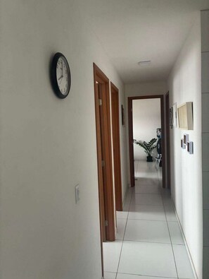 Ein Flur mit einer Uhr an der Wand, Holztüren und einer Pflanze im Hintergrund.
