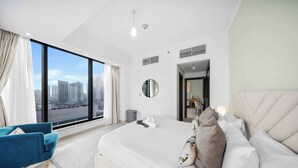 A modern hotel room with a large bed, a blue armchair, a view of the city, and a large window. - Free Housekeeping Visits During Your Stay - Stayshort - Chic 1 BR in Dubai Marina Sleeps 2 (Dubai)