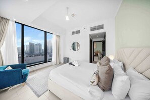 Ein modernes Hotelzimmer mit einem großen Bett, einem blauen Sessel und Blick auf die Stadt, inklusive großem Fenster.