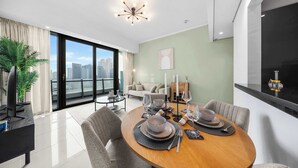 A modern dining area with a round table set for four, a sofa, and a city view through large windows. - Free Housekeeping Visits During Your Stay - Stayshort - Chic 1 BR in Dubai Marina Sleeps 2 (Dubai)