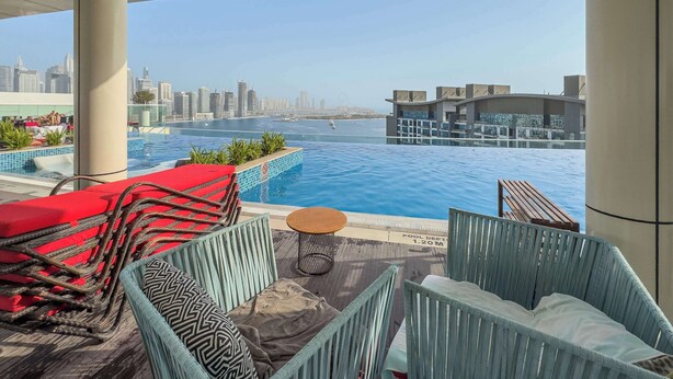A rooftop pool area with lounge chairs, a small table, and a view of a city skyline and water body. - Free Housekeeping Visits During Your Stay - Stayshort - Prime 1 Bedroom Sleeps 2 in Palm Jumeirah (Dubai)