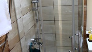 Lasiseinöillä varustettu suihkutila, jossa on valkoinen kylpyamme, pyyheteline ja saippua-annostelija.
