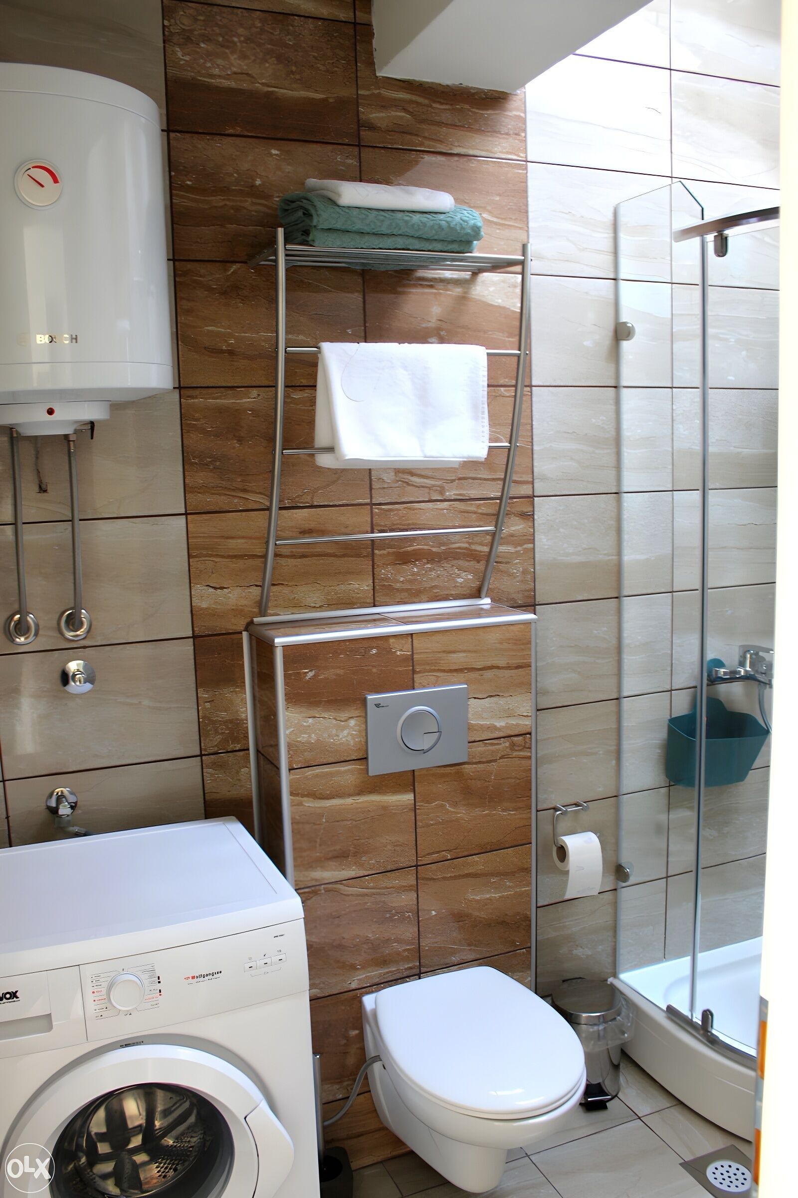 A compact bathroom with a washing machine, toilet, and a shower area.