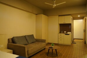 A compact living space with a sofa, a small table with a plant, and a kitchenette area.