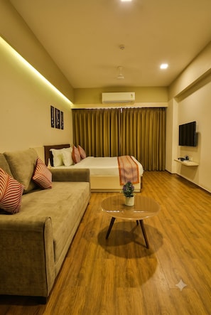 A hotel room with a bed, a sofa, a coffee table, a TV, and a wall-mounted air conditioner.