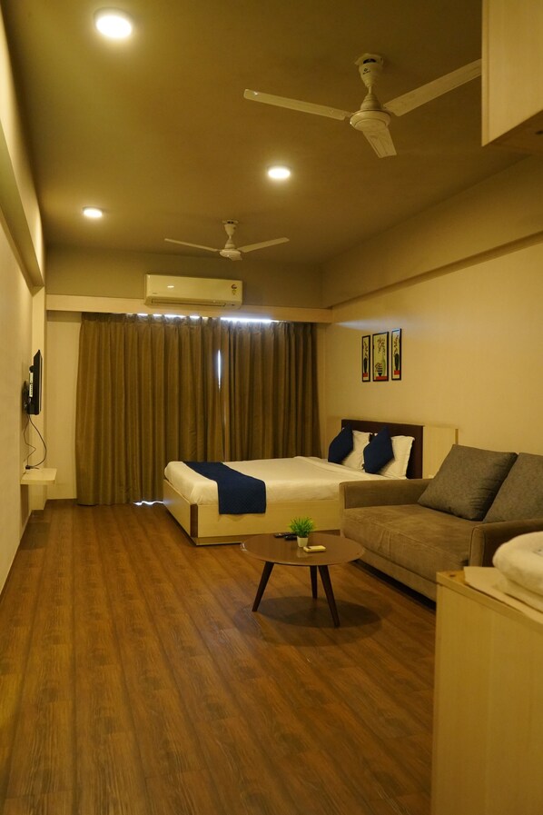 Habitación de hotel con cama, sofá, mesa de centro y ventilador de techo.
