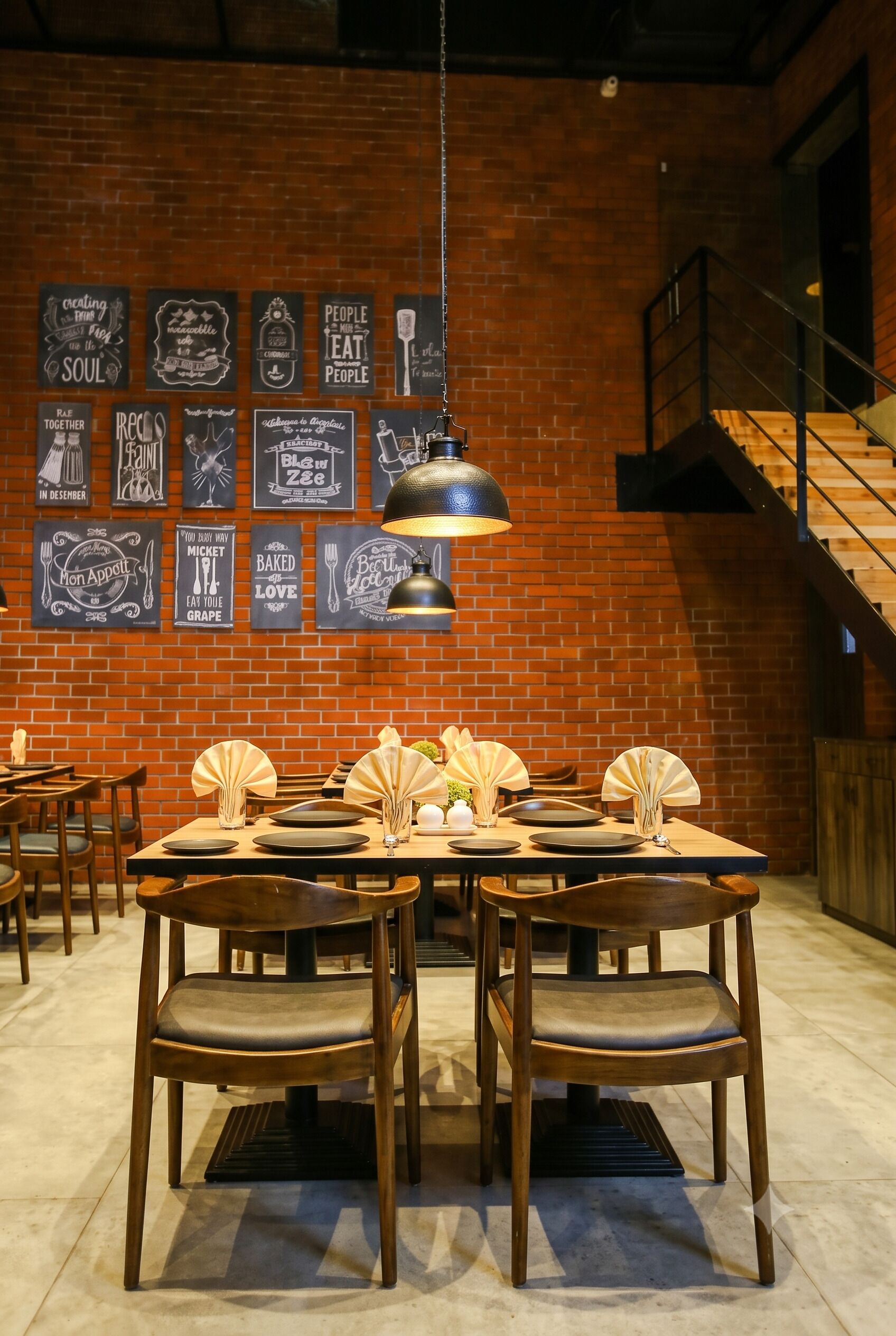 Interior de restaurante con paredes de ladrillo, varias mesas dispuestas con platos y cubiertos, y una escalera al fondo.